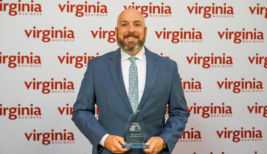 Man in a blue suit smiles while holding a glass award, with a Virginia Business backdrop behind him.